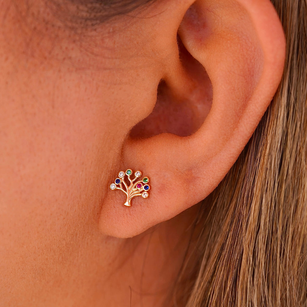 A close-up of a woman wearing the 14K gold Tree of Life earrings, with the delicate studs resting gracefully on her earlobes. The polished gold and radiant Cubic Zirconia catch the light, adding a subtle yet sophisticated touch to her look.
