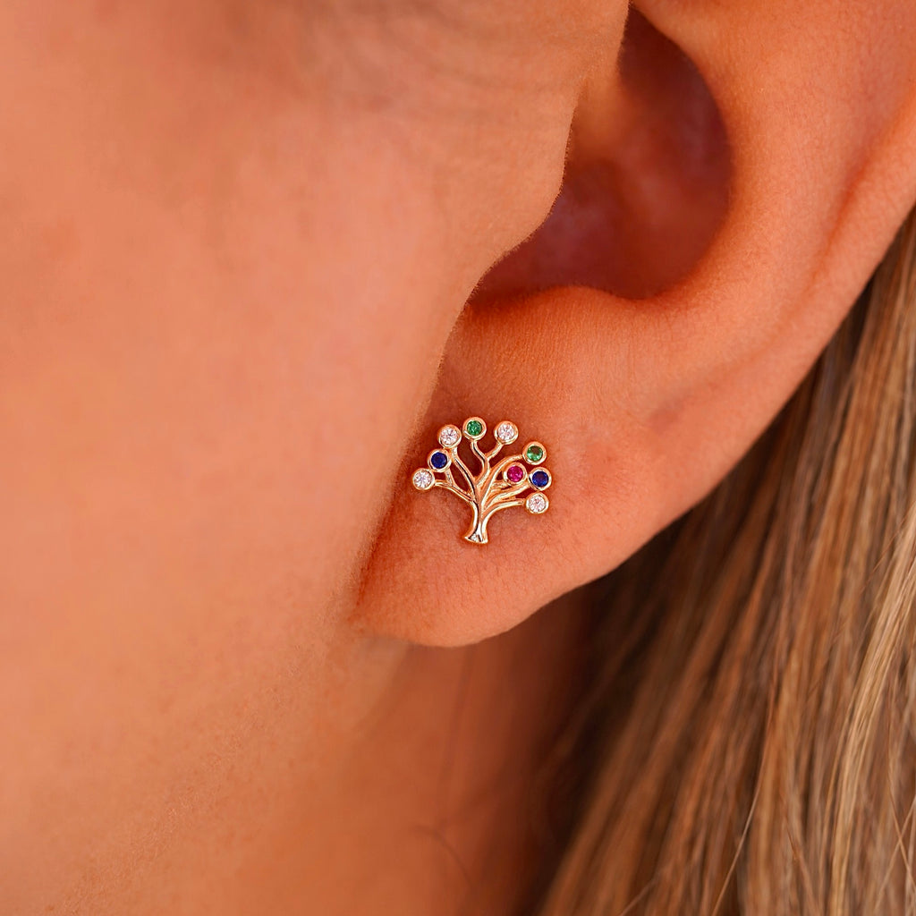 A close-up of a woman wearing the 14K gold Tree of Life earrings, with the delicate studs resting gracefully on her earlobes. The polished gold and radiant Cubic Zirconia catch the light, adding a subtle yet sophisticated touch to her look.