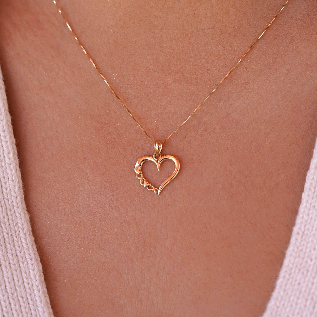Model wearing a delicate 14K gold heart charm on a dainty chain, the pendant resting gracefully near the collarbone.