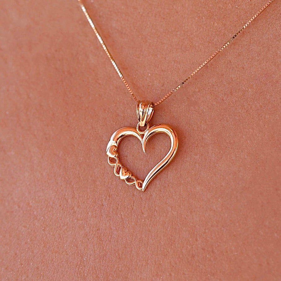 Model wearing a delicate 14K gold heart charm on a dainty chain, the pendant resting gracefully near the collarbone.