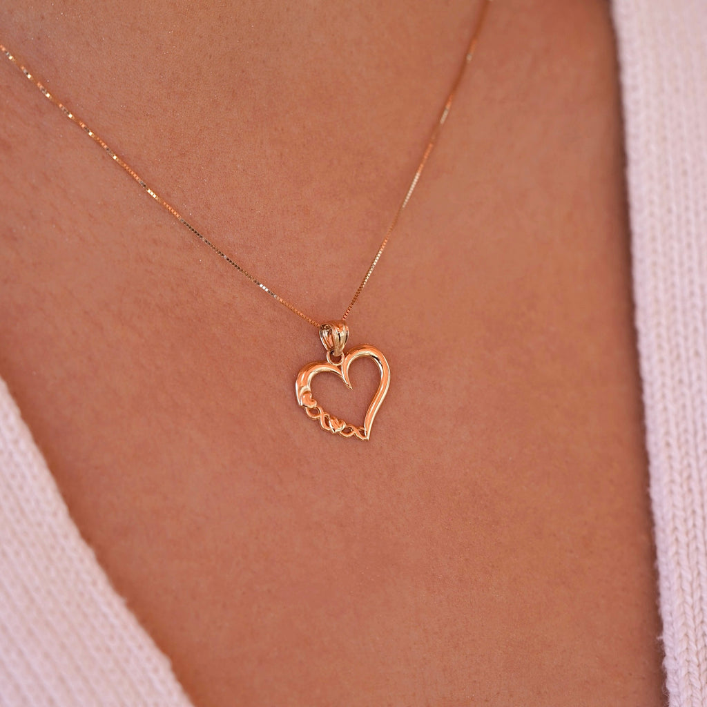 Model wearing a delicate 14K gold heart charm on a dainty chain, the pendant resting gracefully near the collarbone.