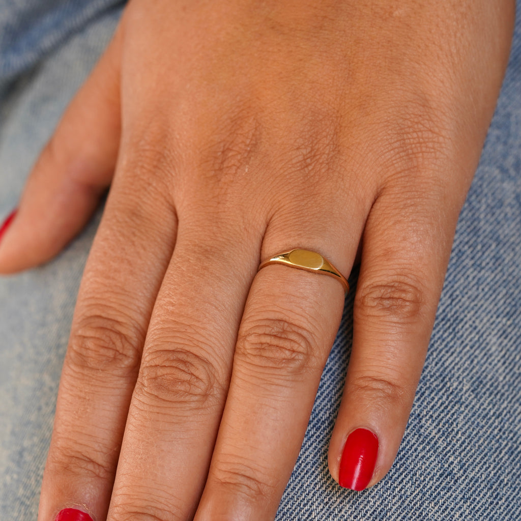 Model wearing a 14K Solid Gold Signet Ring, showcasing its polished finish and bold design on their hand. Shot from a top-down angle to highlight the ring sleek surface.
