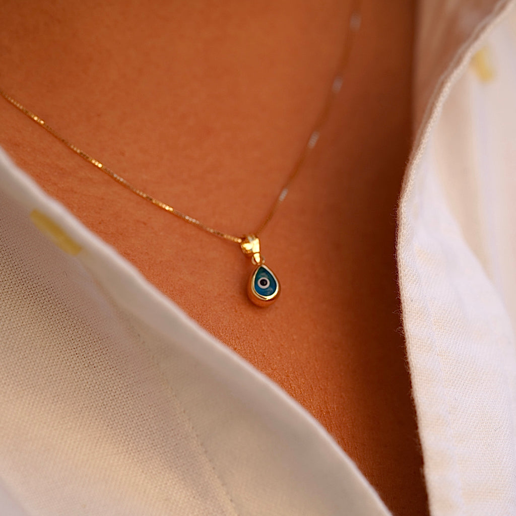 A model wears the 14K Gold Tiny Tear Evil Eye Charm with the vibrant blue eye, adding a touch of protection and elegance to her necklace.
