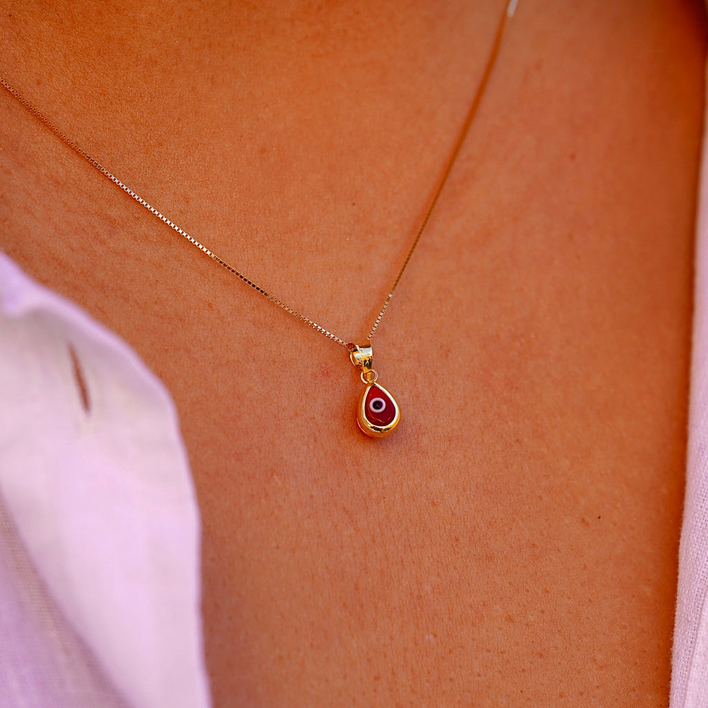 A model wears the 14K Gold Tiny Tear Evil Eye Charm with the vibrant Red eye, adding a touch of protection and elegance to her necklace.