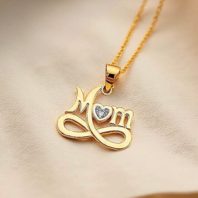 14K Gold Mom Pendant resting on textured, off-white fabric, capturing the pendant's soft golden glow and elegant detail.
