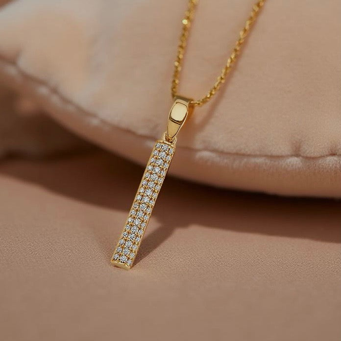 Elegant 14K gold CZ bar pendant resting on a soft, beige textured cloth, showcasing its shine and delicate craftsmanship.