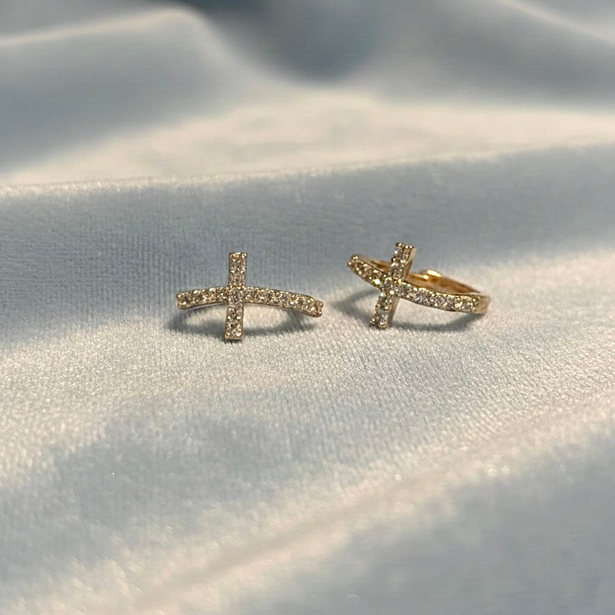 14K solid gold curved CZ cross Huggies earrings displayed on a light blue velvet cloth, highlighting the curved cross shape and CZ sparkle.