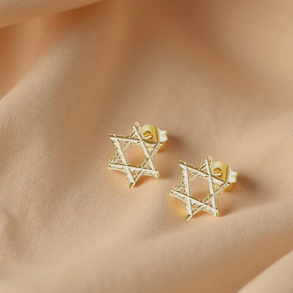 Close-up of Star of David gold studs resting on a textured cream fabric, highlighting their fine detail and elegant style.