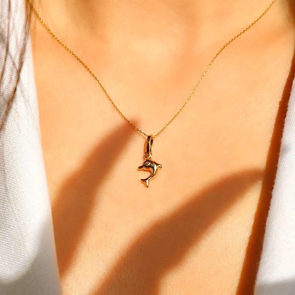 Model wearing the 14K yellow gold dolphin pendant on a fine chain, demonstrating its dainty size and stylish appeal.