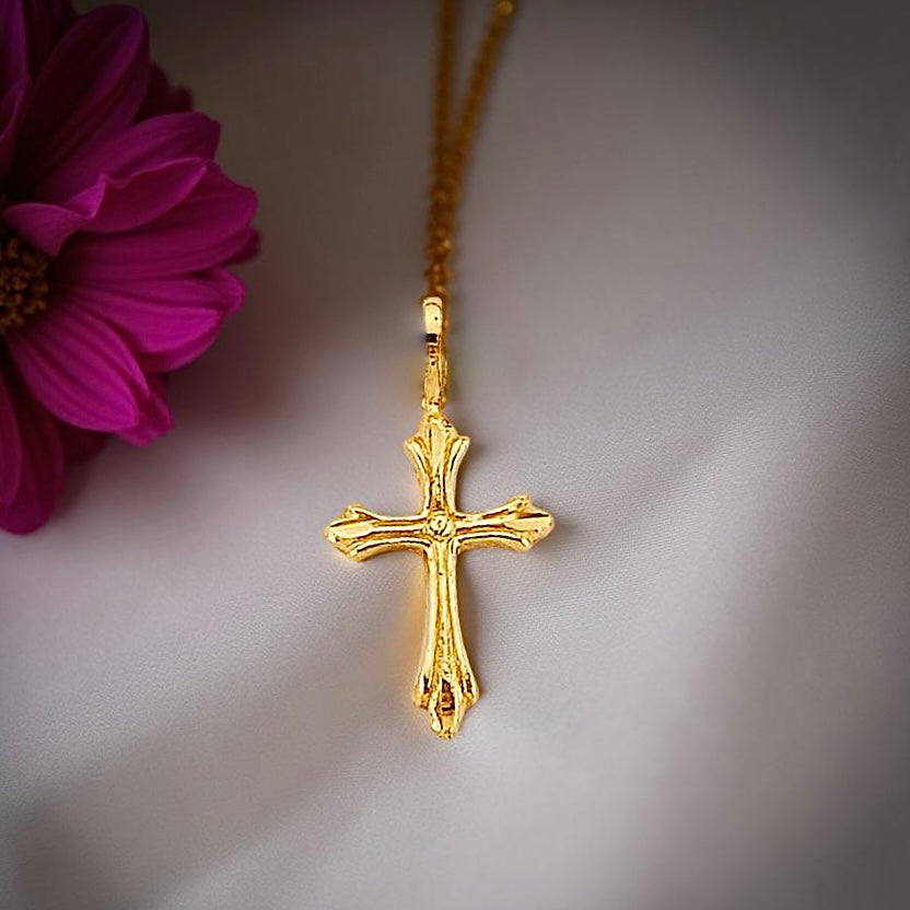 Dainty 14K yellow gold cross pendant displayed on soft off-white cloth, highlighting its classic shape and radiant finish.