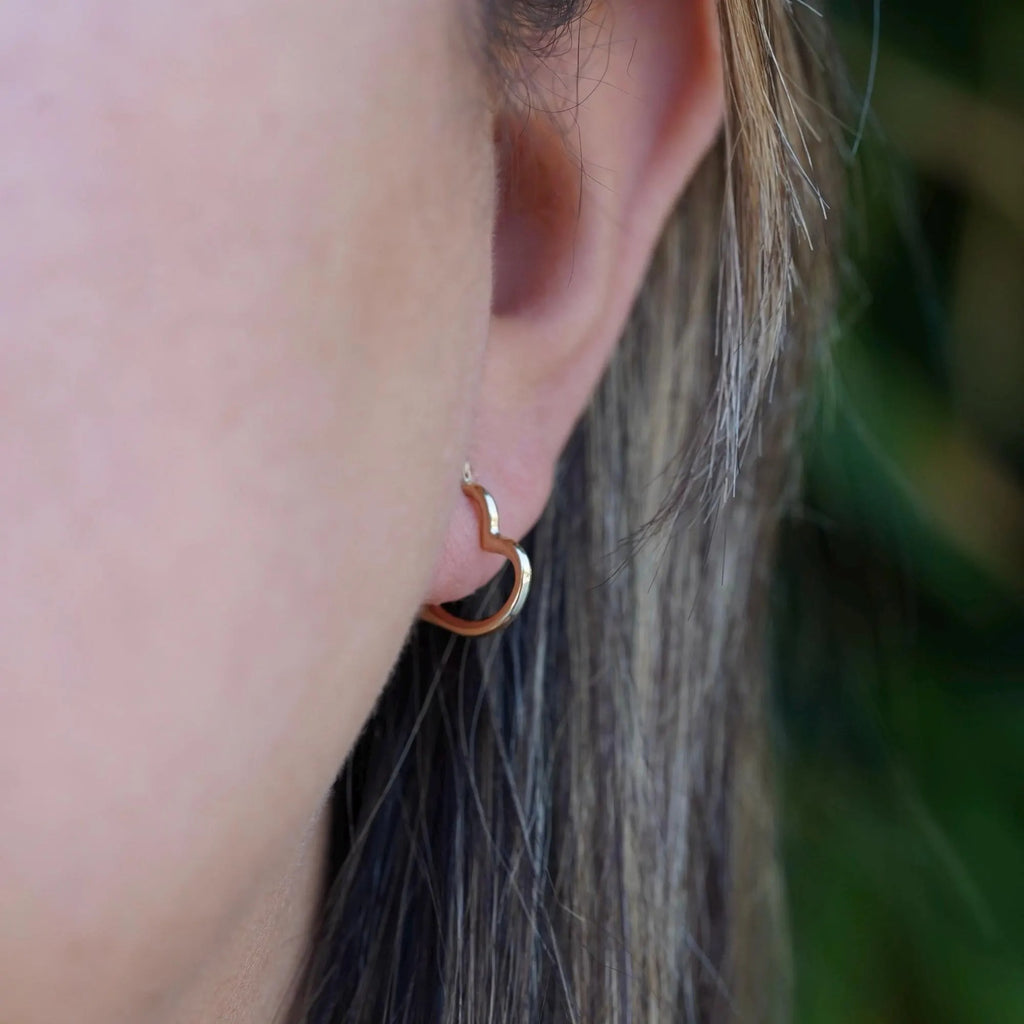 Model wearing dainty 14K yellow gold heart hoop earrings, with a radiant shine, highlighting the elegance and minimalist design of the earrings against a soft, natural background.