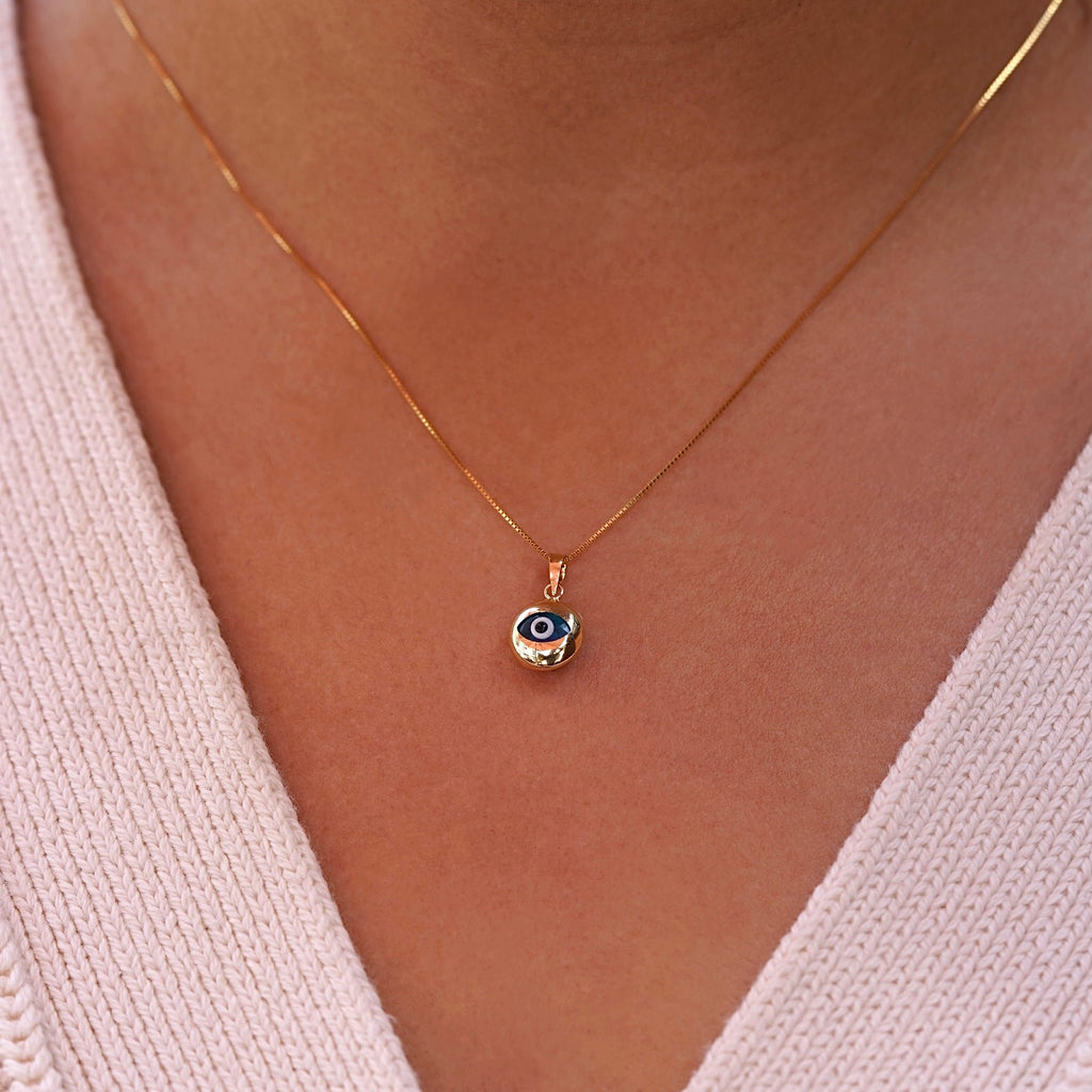 A model wearing a 14K yellow gold evil eye pendant with a blue zirconia center on a fine gold chain, resting elegantly at her collarbone. The polished gold finish reflects light beautifully, highlighting the pendant’s delicate craftsmanship, symbolic protection, and subtle luxury from Tehrani Jewelry.