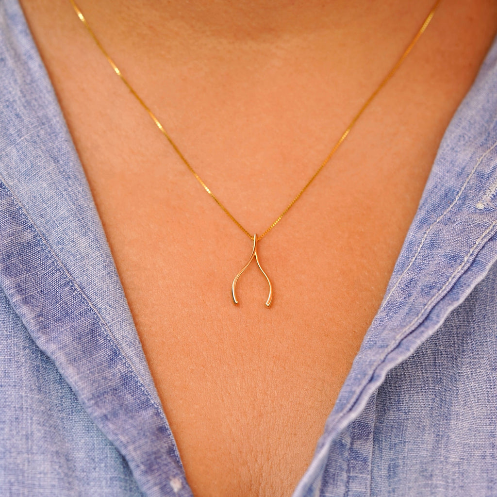 Model wearing the 14K gold wishbone pendant on a delicate chain, demonstrating its dainty size and elegant everyday look.