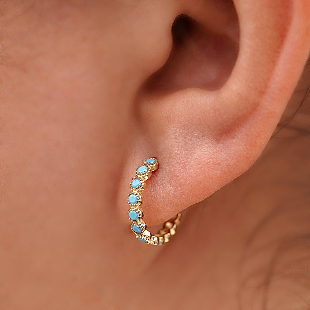 Side profile of a model wearing 14K yellow gold round turquoise Huggies earrings, highlighting the delicate hoops with turquoise accents hugging her earlobe, styled with casual outfit for an elegant everyday look.