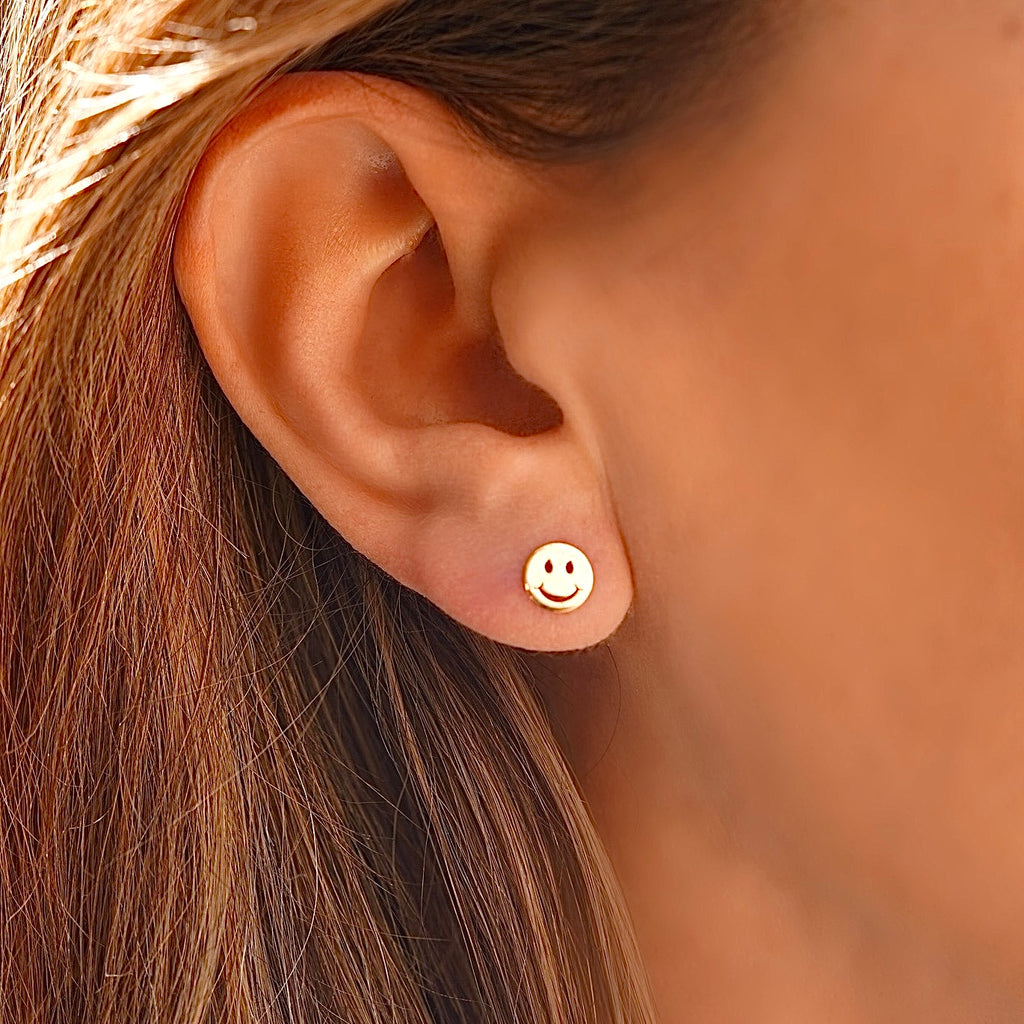 Close-up of a model wearing the 14K Yellow Gold Smiling Emoji Stud Earrings, showcasing their fun and playful design with a secure screw-back closure.