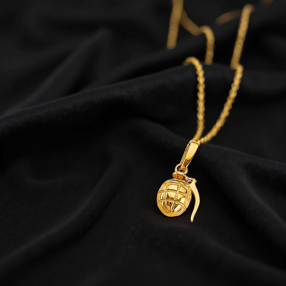 Miniature gold grenade charm placed on a black fabric, showing off its realistic shape and reflective surface.