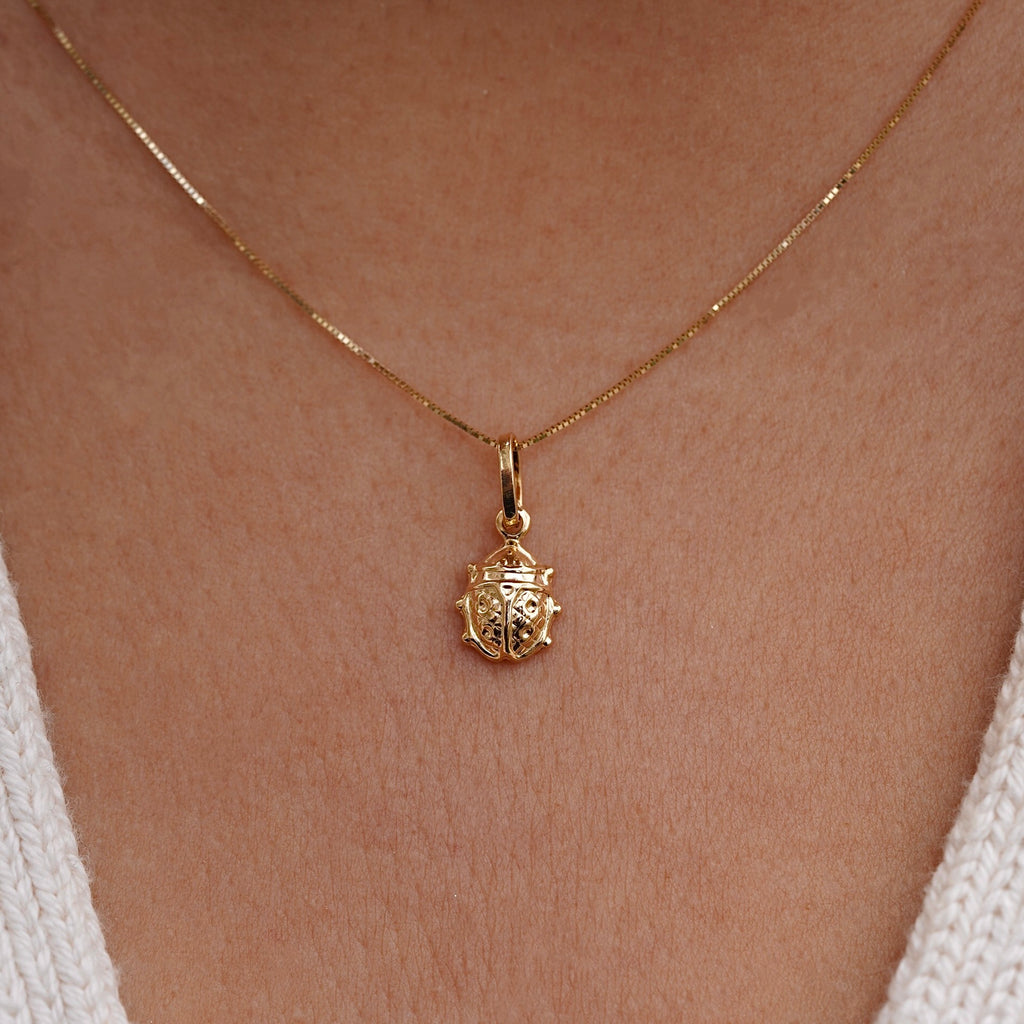Model wearing a delicate 14K gold ladybird pendant on a fine chain, showcasing its dainty size and polished gold shine against the neckline.