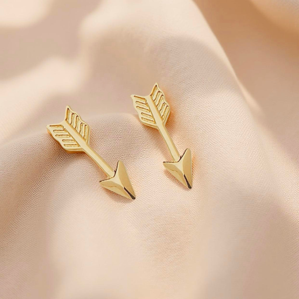 Pair of 14K gold arrow earrings displayed on neutral fabric, showcasing their minimal and sleek form with a refined polished shine.