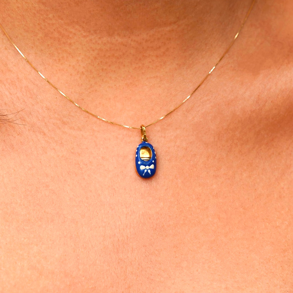 A model wearing a delicate 14K gold baby shoe pendant with blue enamel on a thin gold chain. The pendant is the focal point, elegantly styled and perfect for daily wear or special occasions, with the model showcasing its charm and grace.