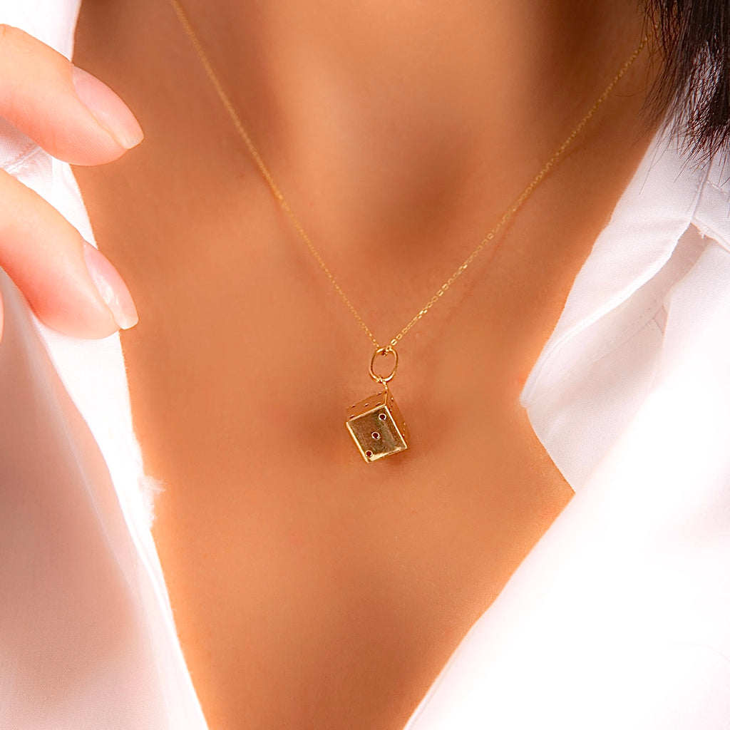 A model is wearing the 14K Gold Dice Pendant on a delicate chain, with the charm resting elegantly against the collarbone, adding a subtle yet playful touch to the outfit.