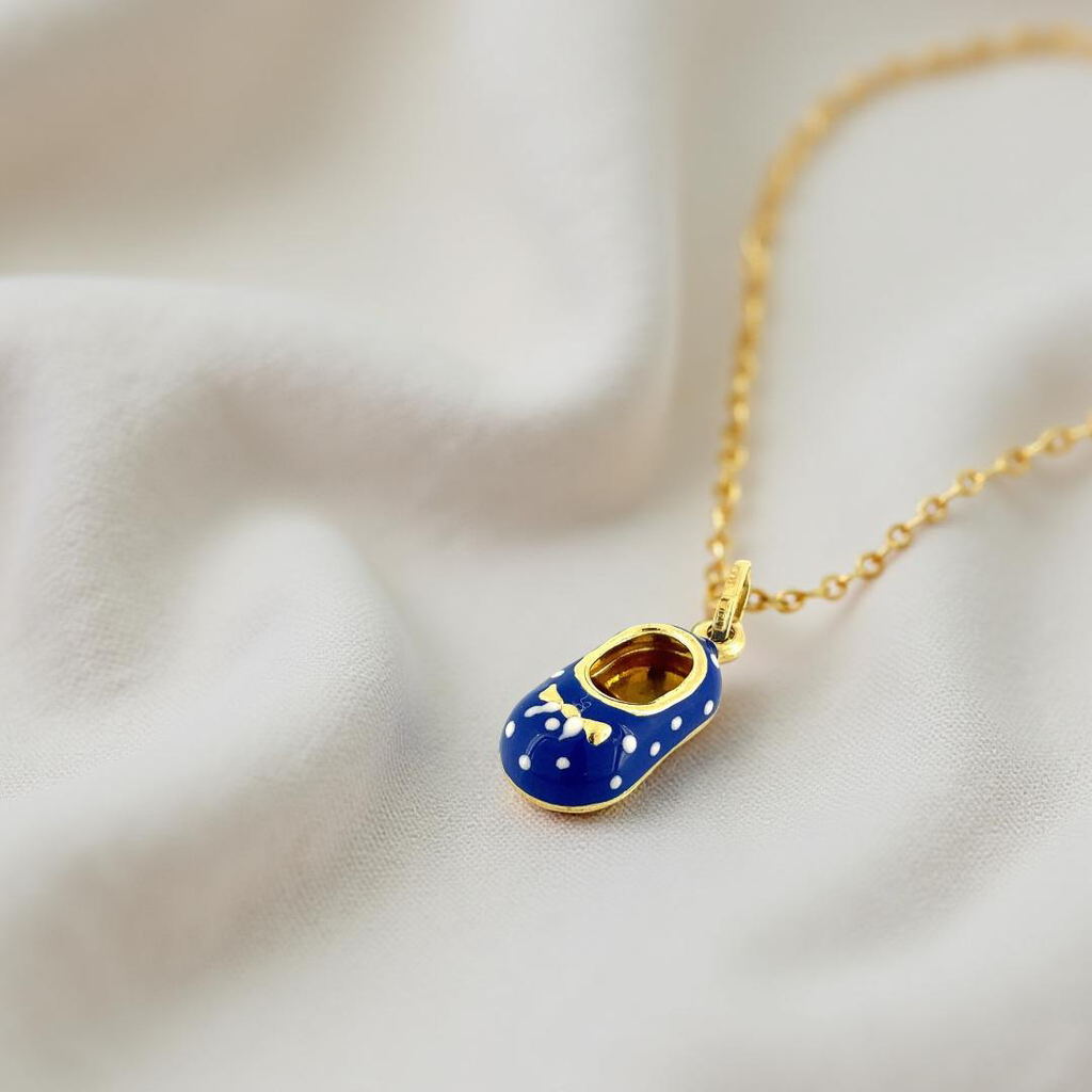 14K gold baby shoe pendant with blue enamel detail, elegantly displayed on off-white textured fabric background.