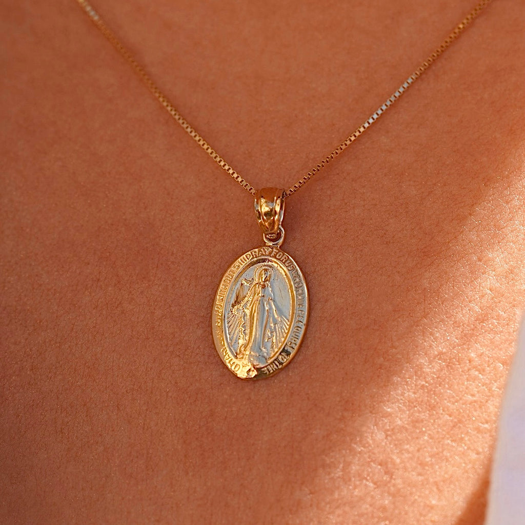 Model wearing a 14K gold Milagrosa pendant on a fine gold chain, the lightweight medallion resting at the collarbone, adding a subtle yet meaningful touch of faith.
