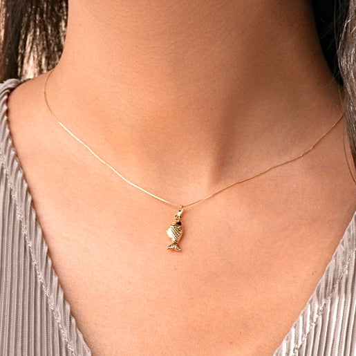 A woman wearing the 14K Gold Fish Charm Pendant on a delicate gold chain, highlighting its elegant shine and dainty size as it rests gracefully on her collarbone.