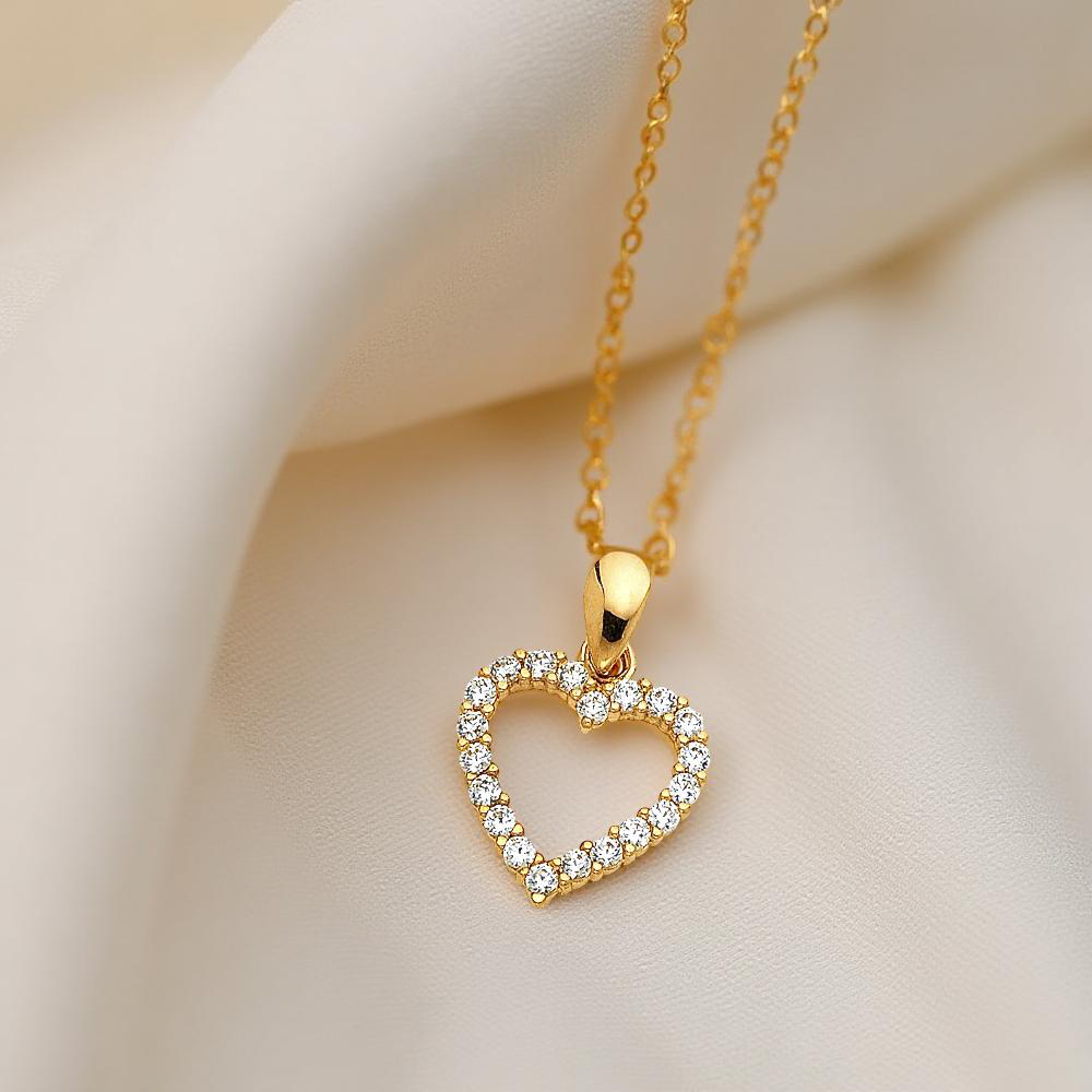 Close-up of the 14K Gold Heart Pendant with CZ stones resting gently on a textured off-white cloth, emphasizing the pendant's warm gold tones and shimmering stones in natural light.