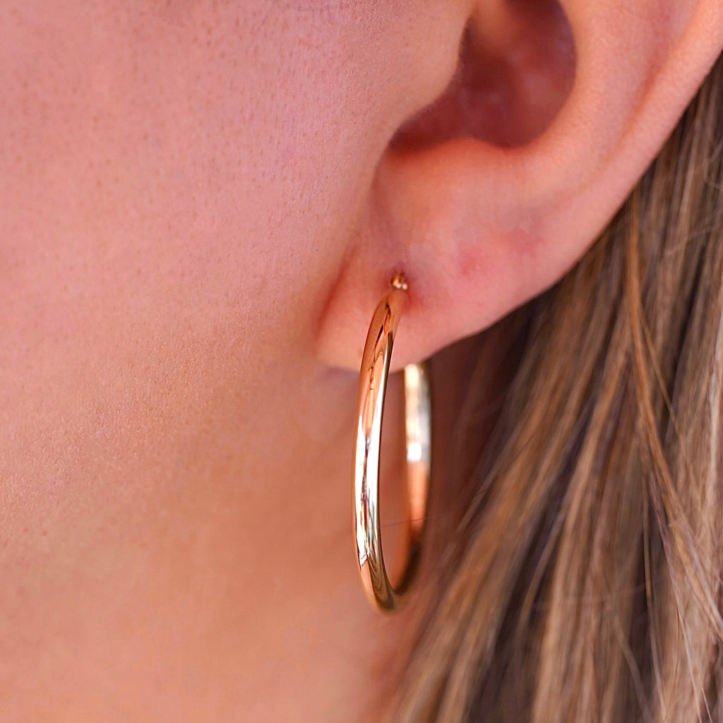A stylish woman wearing 14K gold hoop earrings in yellow and white gold, adding a touch of sophistication to her everyday look.