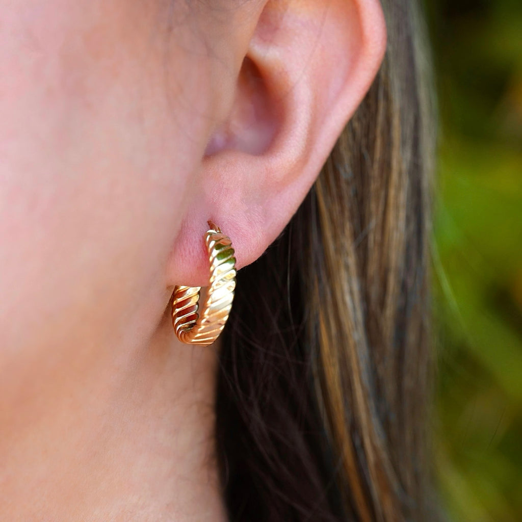 A woman elegantly wearing a pair of 14K solid gold Huggies hoop earrings. The 20mm hoops hug her earlobes perfectly, complementing her effortless style with a touch of timeless luxury.