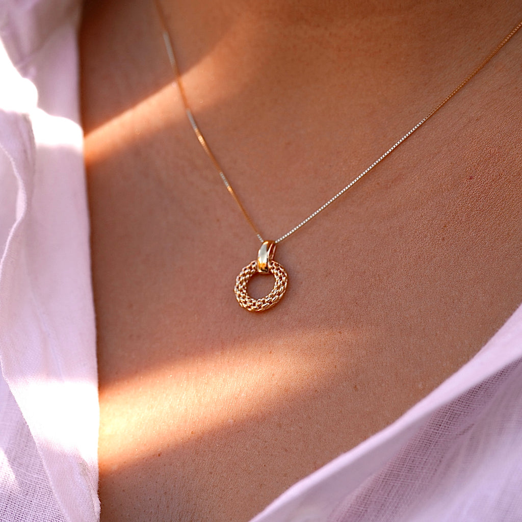 A woman wears the 14K gold mesh pendant on a dainty gold chain, the intricate filigree design resting gracefully against her collarbone. The lightweight and elegant pendant adds a timeless touch to her outfit.