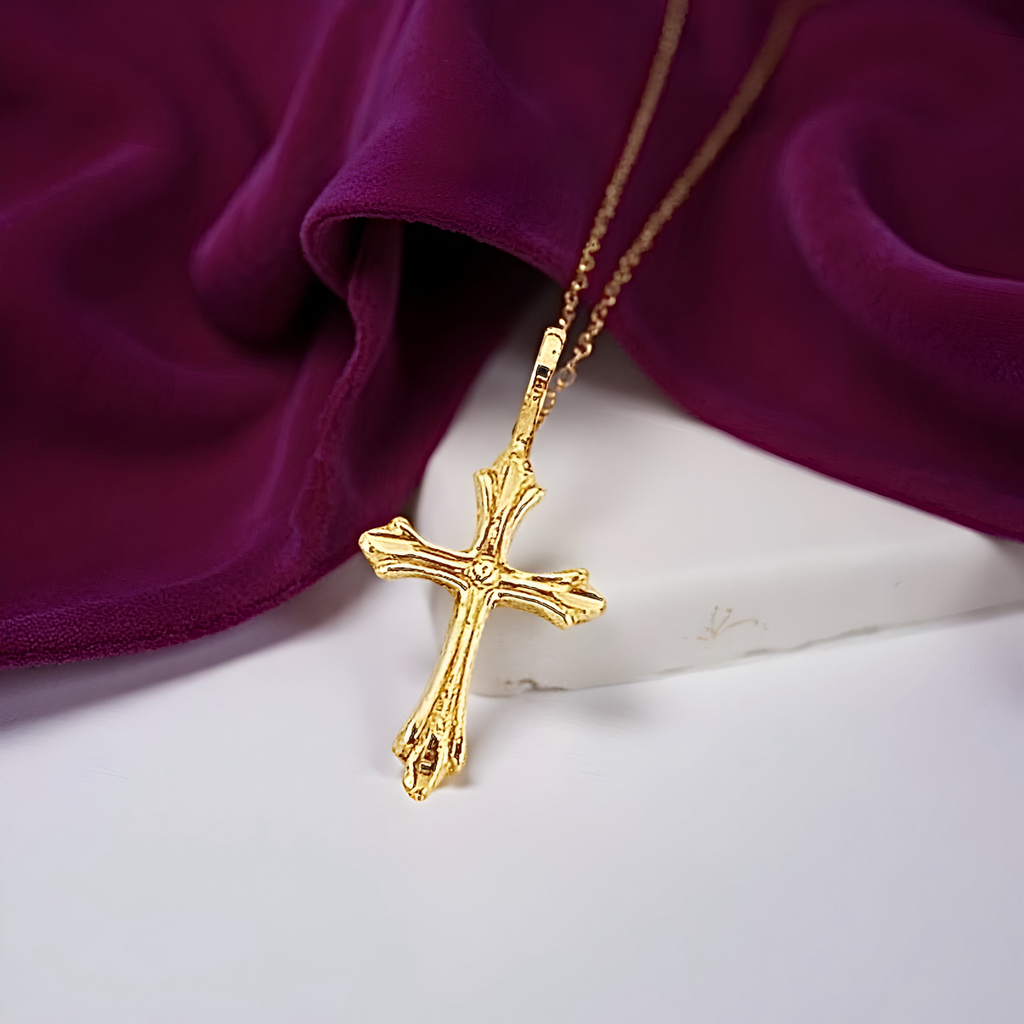 Minimalist gold cross charm resting on white surface and magenta fabric, reflecting the light and showing its polished craftsmanship.