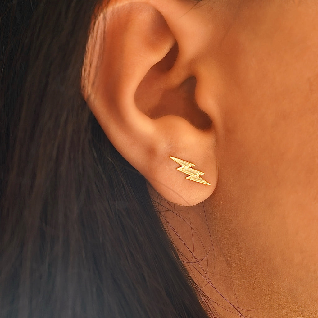 Model wearing 14K gold thunderbolt earrings, showcasing their trendy lightning bolt shape and dainty fit on the ear.