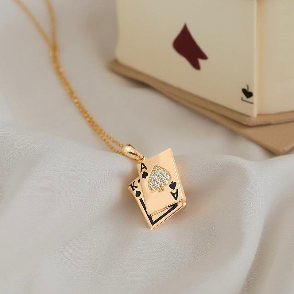 14K gold CZ Spade A & K card pendant resting on textured off-white fabric background, showcasing sparkling details.