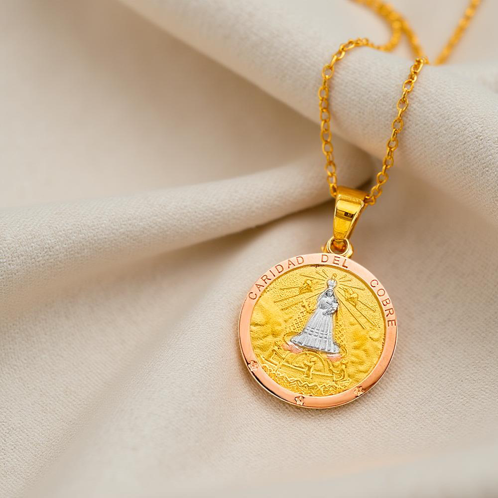 Elegant Cuban Caridad del Cobre pendant in rose, white, and yellow gold, placed on a neutral linen cloth, highlighting the intricate detailing and rich spiritual symbolism of this religious charm.