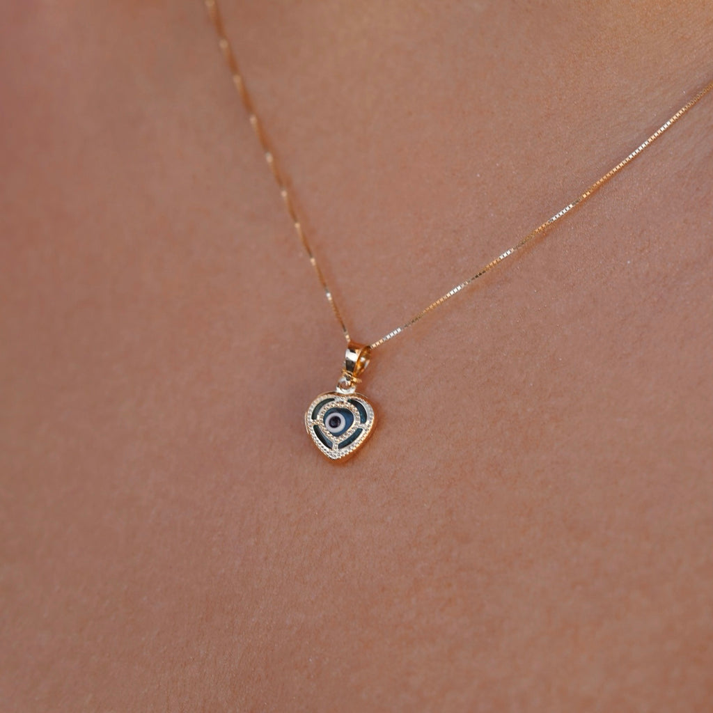 Model wearing a 14K yellow gold heart pendant with an evil eye center, showcasing elegant shine and dainty design against the skin.