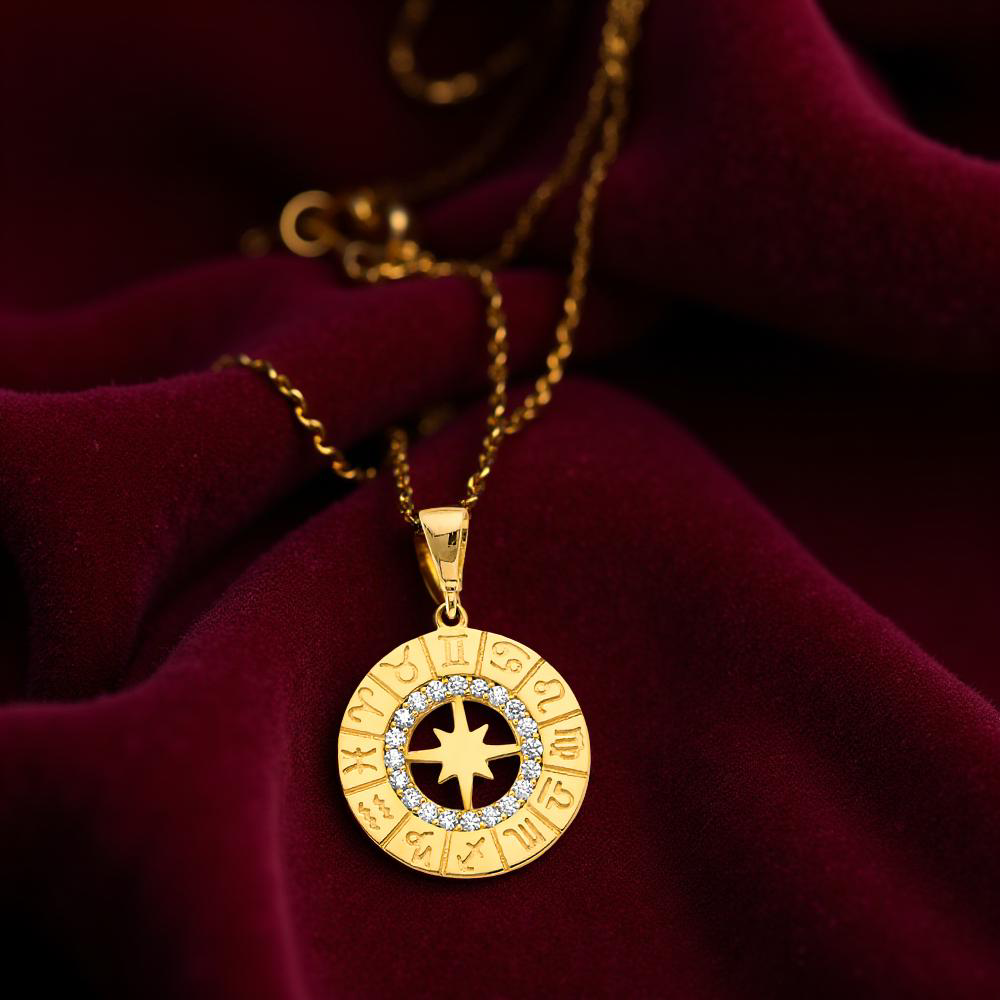 14K two-tone gold zodiac pendant resting on a dark red velvet cloth, displaying shimmering cubic zirconia accents.