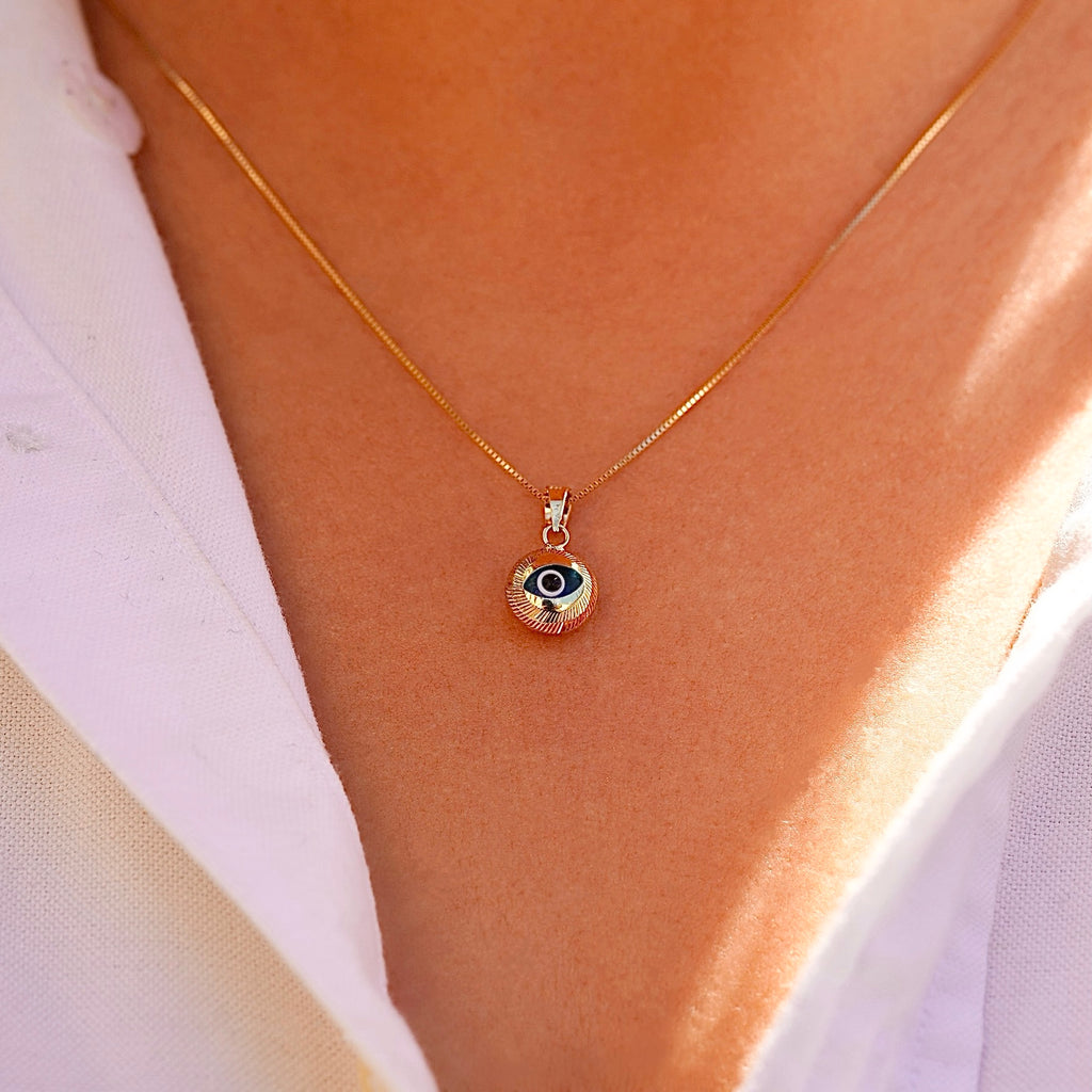 A model wears the 14K gold evil eye pendant with blue center on a fine chain, showcasing its dainty size and symbolic beauty as it rests just below the collarbone.