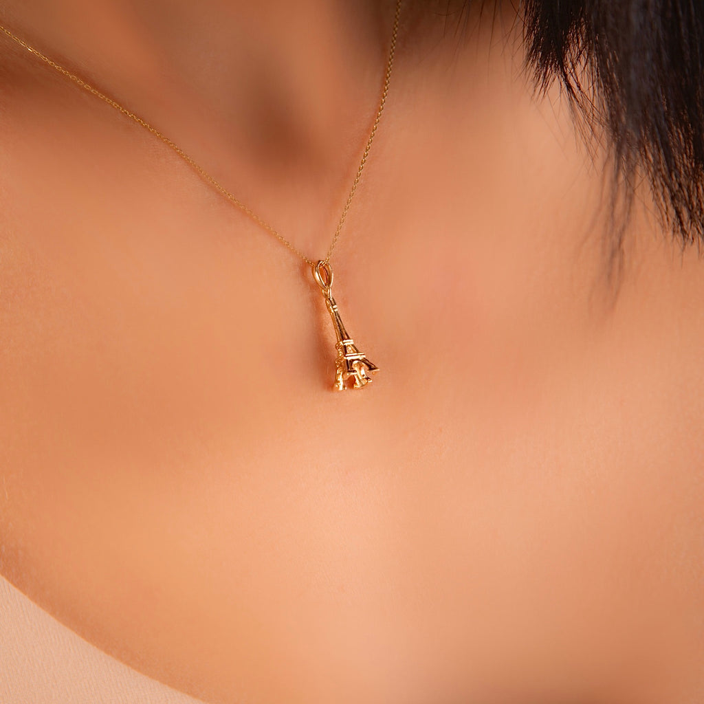 A woman elegantly wearing the 14K gold Eiffel Tower pendant on a delicate chain, adding a touch of Parisian charm to her outfit.