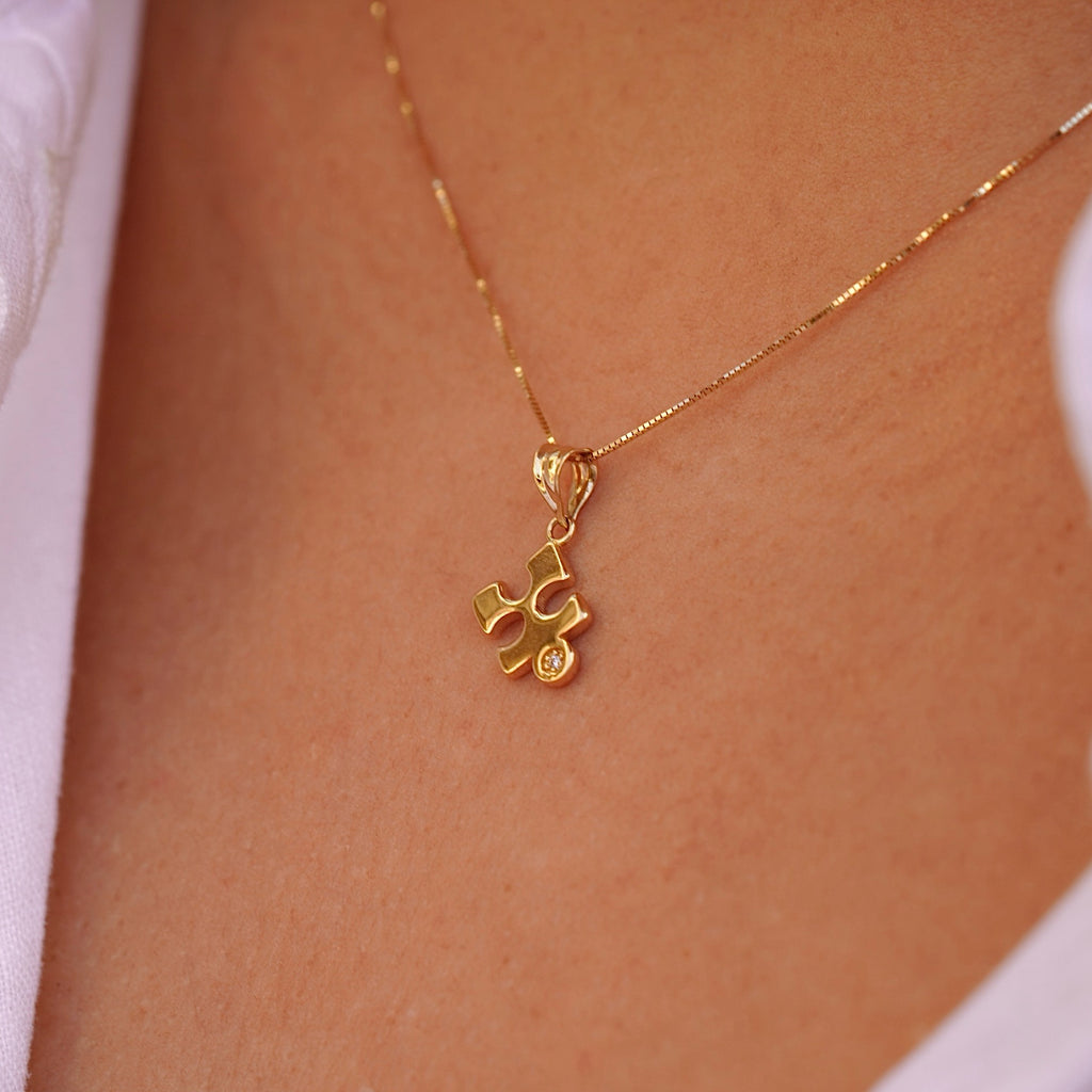 A model gracefully wears the 14K gold puzzle piece pendant on a fine chain, showcasing its subtle elegance and timeless design. The charm rests beautifully against the skin, adding a touch of meaning and sophistication to any outfit.