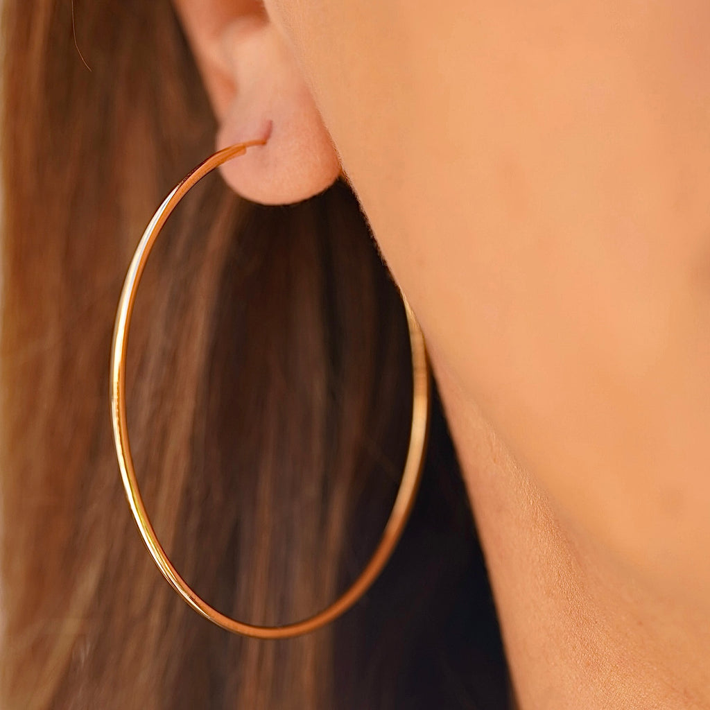 A model wearing 14K Yellow Gold 1.5mm Endless Hoop Earrings (55mm), highlighting their large size and elegant style for everyday wear.