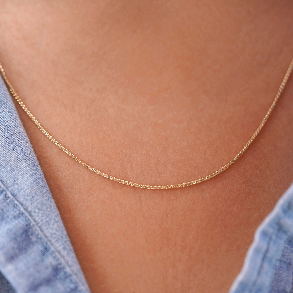 A model wearing a 14K yellow solid gold wheat chain necklace with 1.5mm flat open links, styled with a casual outfit to show the necklace’s versatility for both everyday and formal wear.