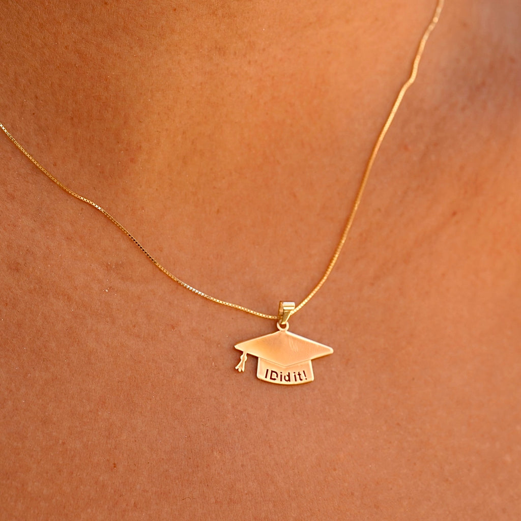 A model elegantly wears the 14K solid gold graduation cap pendant on a delicate chain, showcasing its brilliant shine and meaningful design. The charm rests beautifully against the skin, making it a perfect way to commemorate this special milestone.