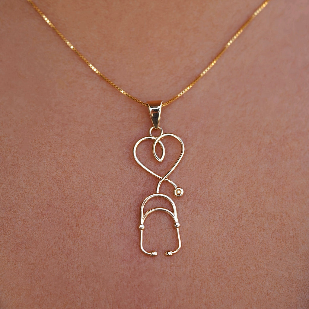 Close-up of the stethoscope pendant worn by a model, highlighting the charm's detailed craftsmanship and how it elegantly rests on the chest.