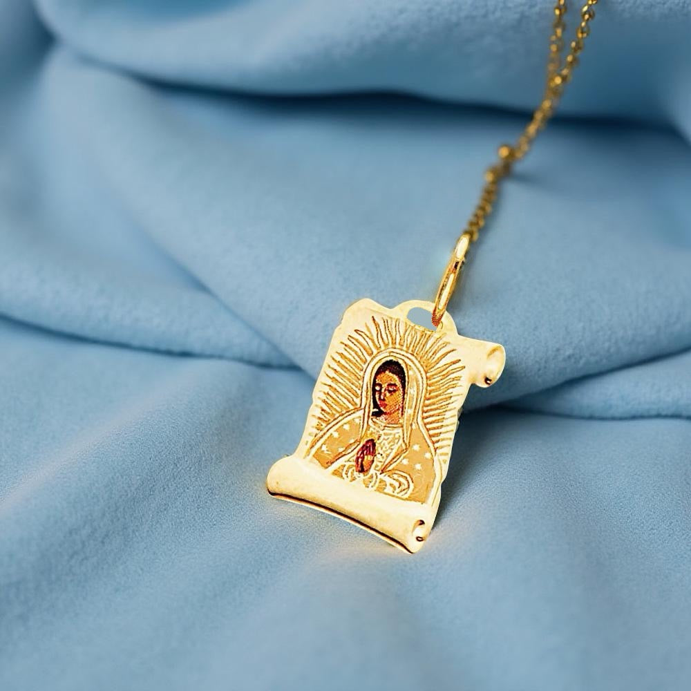 14K yellow gold medium Virgin Mary Guadalupe pendant (16mm x 13mm) resting gently on a blue velvet fabric, emphasizing its polished gold surface and finely detailed sacred design. The soft texture of the velvet contrasts beautifully with the shine of the charm, enhancing its elegance and spiritual symbolism.