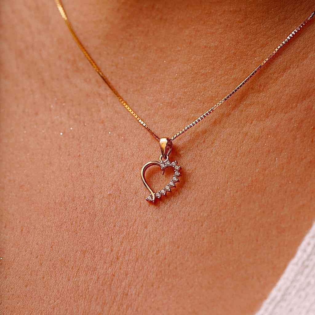 A delicate 14K Gold CZ Heart Pendant worn on a fine chain, elegantly resting against a model’s neckline, highlighting its dainty and elegant design.