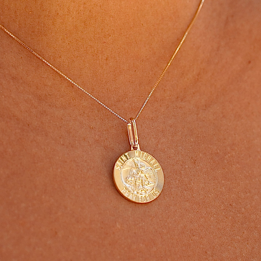 A woman wearing the 14K gold Saint Michael pendant on a delicate chain, resting elegantly against his chest, emphasizing its spiritual significance and timeless elegance.