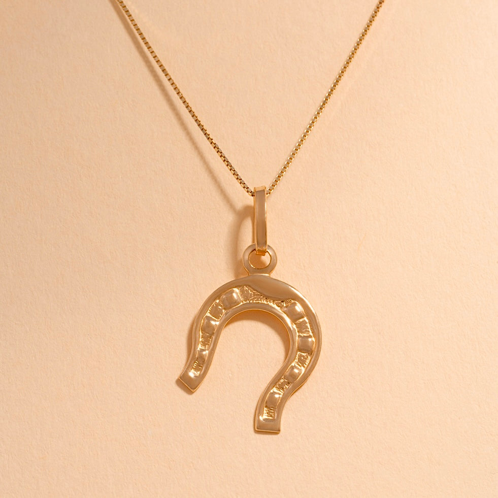 14K Solid Gold Horseshoe Charm with a polished finish, symbolizing good luck and protection, placed against a plain background.