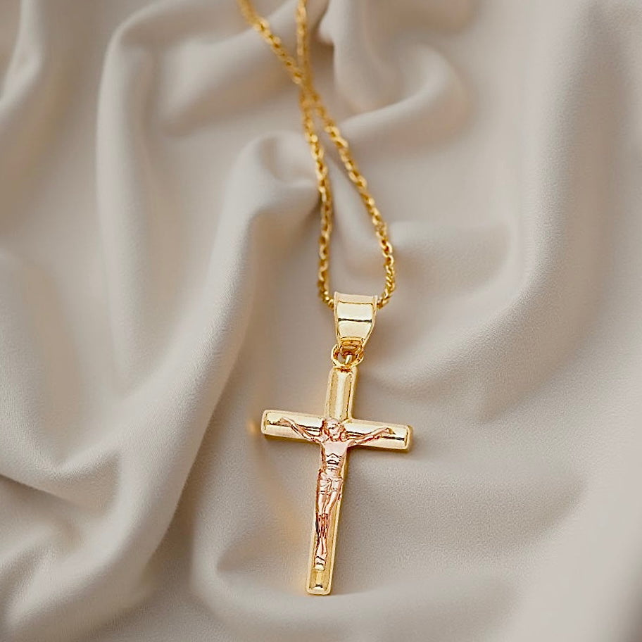 Close-up of a 14K two-tone crucifix pendant resting on a soft off-white fabric, highlighting the intricate figure of Christ and polished cross design.