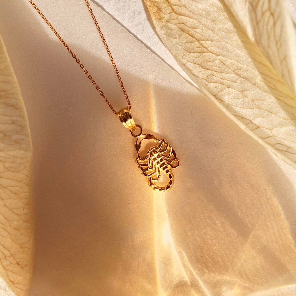 A 14K real gold scorpion pendant displayed against a cream backdrop, highlighting its polished finish, intricate detailing, and dainty size.
